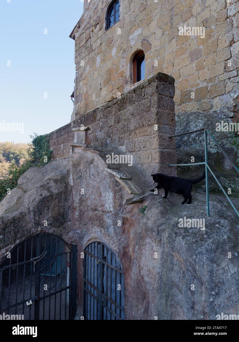 Black cat beside a gated grotto area in the historic town of Calcata, Lazio Region, Italy, December 3rd 2023 Stock Photo