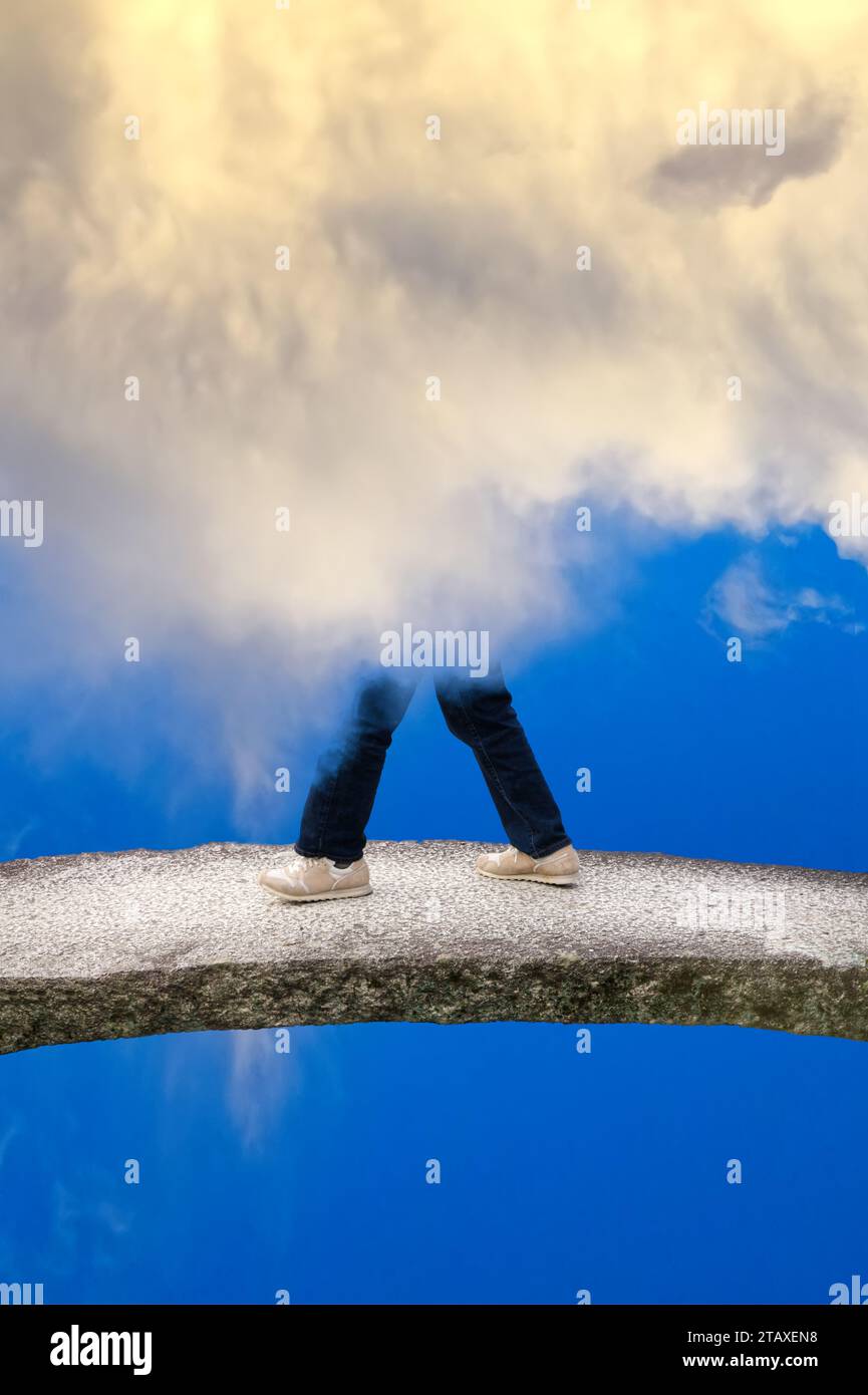 Man walking on the bridge over the empty space wreathed in the clouds Stock Photo