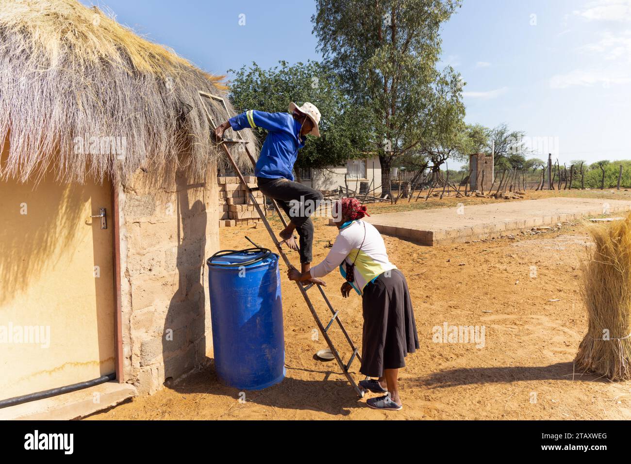 housework in african village, woman coming down the ladder after fixing the thatched roof, another woman helping Stock Photo