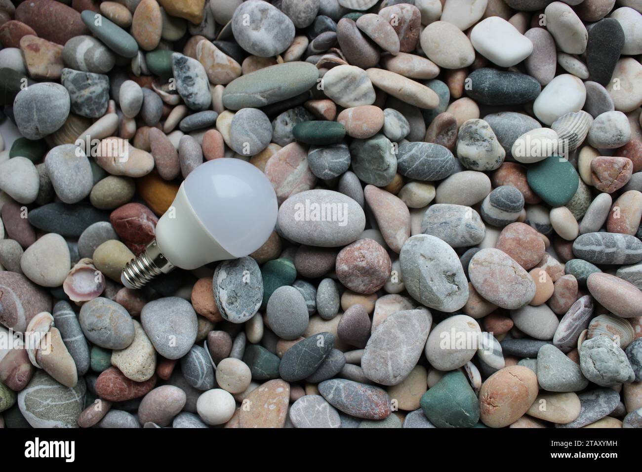 White Plastic Economy Bulb With Metal Base On A Round Rocks Background Stock Photo