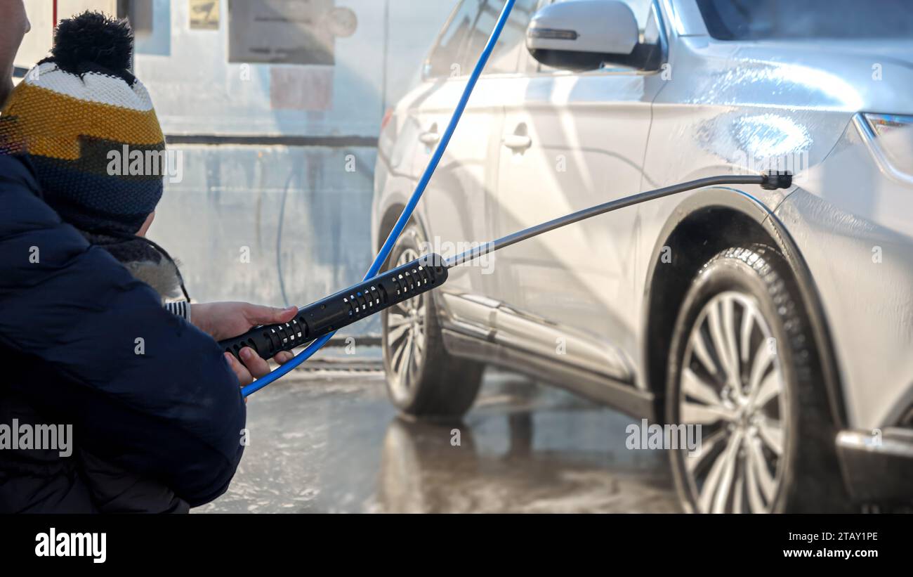 Closeup of man with baby boy washing car at carwash with water jet