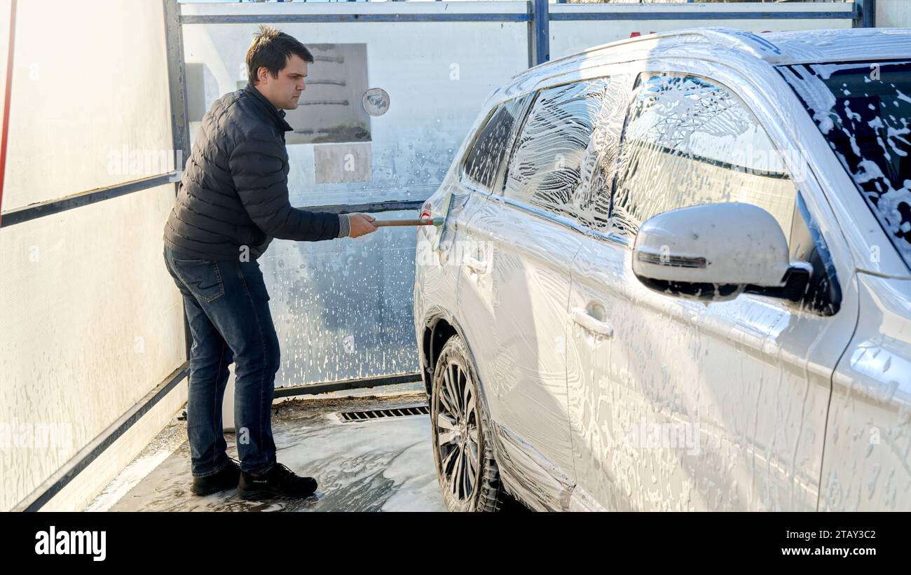 Young man washing his car at selfservice carwash. Automobile care