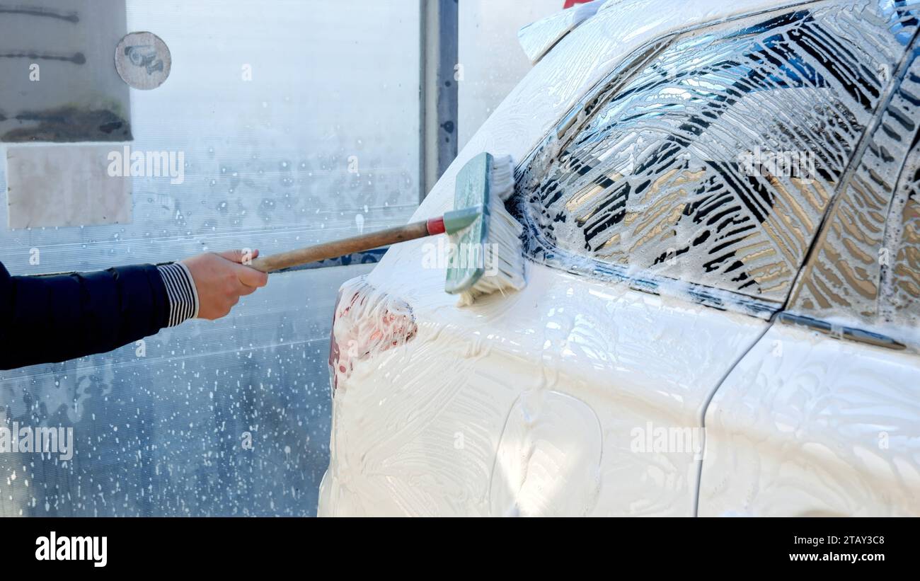 Closeup of man cleaning his dirty car with soap foam and brush. Automobile care, transport