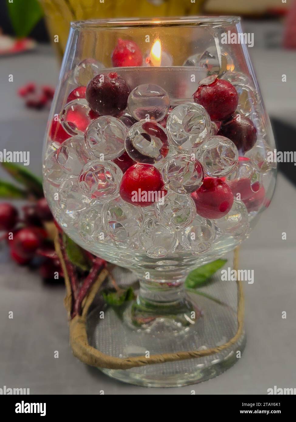 Christmas decorations of candles, cranberries, beads, greenery, and glass goblets grace the table in preparation for a Christmas party or meal. Stock Photo