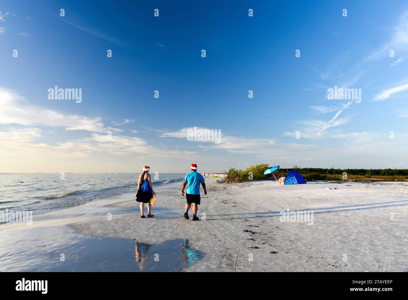 A couple dressed in matching Santa hats enjoy a walk on the beach on Christmas Day at Fort De Soto County Park near St. Petersburg, Florida. Stock Photo
