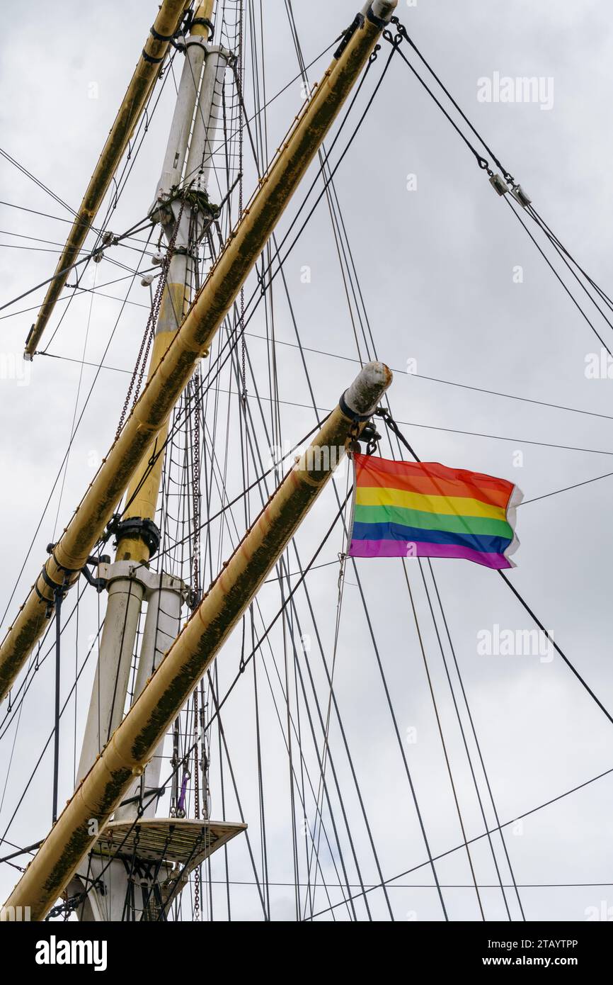 Historic ship mast and rigging with a rainbow pride flag flying in