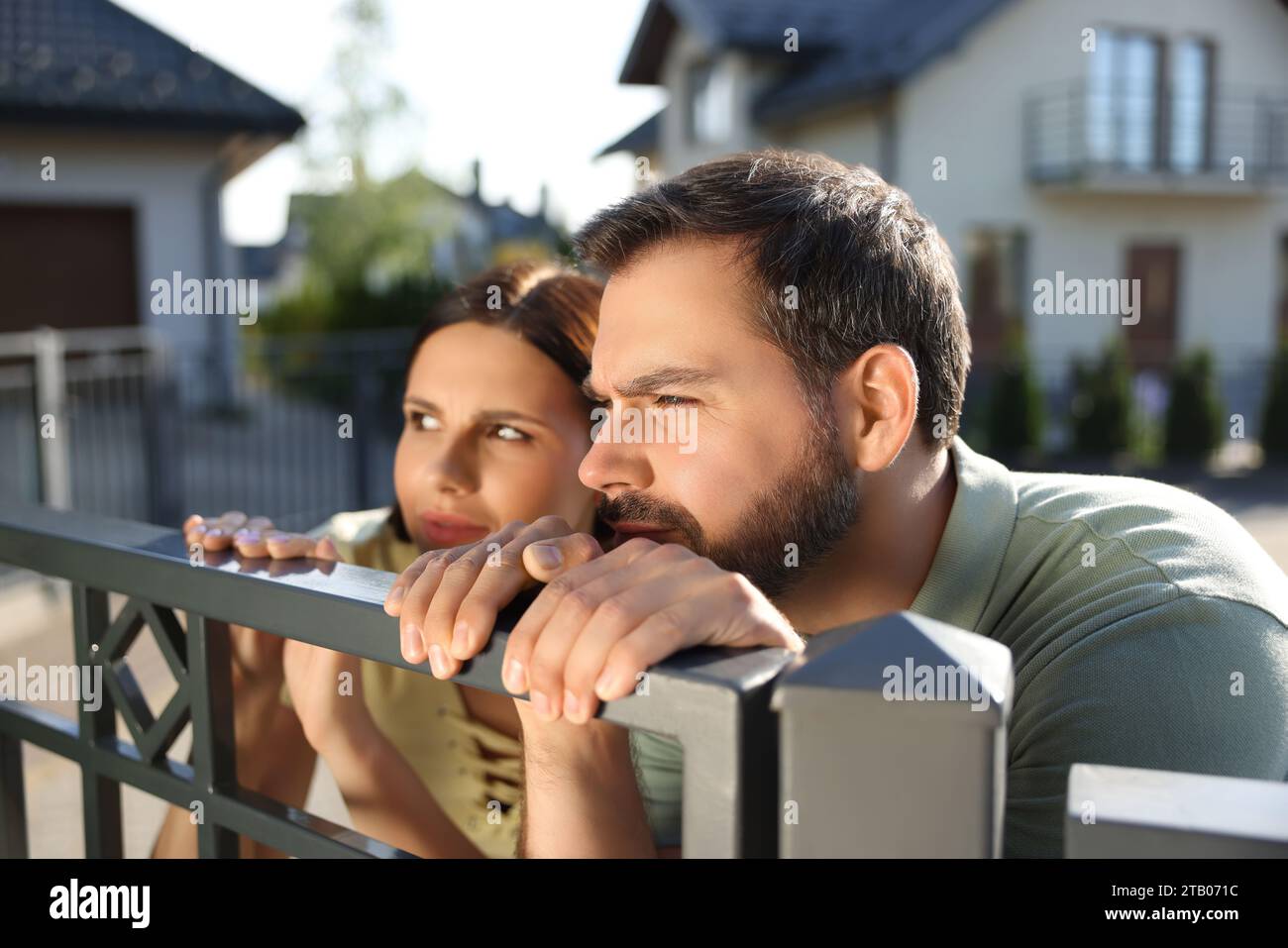 Concept of private life. Curious couple spying on neighbours over fence outdoors Stock Photo