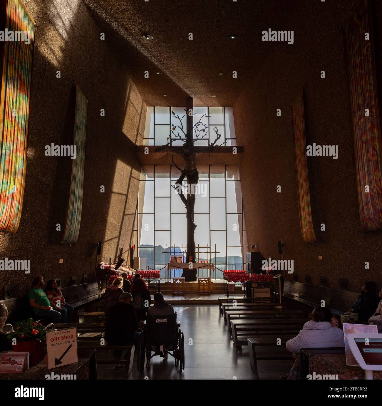 People Praying Inside Famous Modern Chapel Of The Holy Cross with Altar and Jesus Christ Crucifix by Big Glass Window. Sedona, Arizona Southwest USA Stock Photo