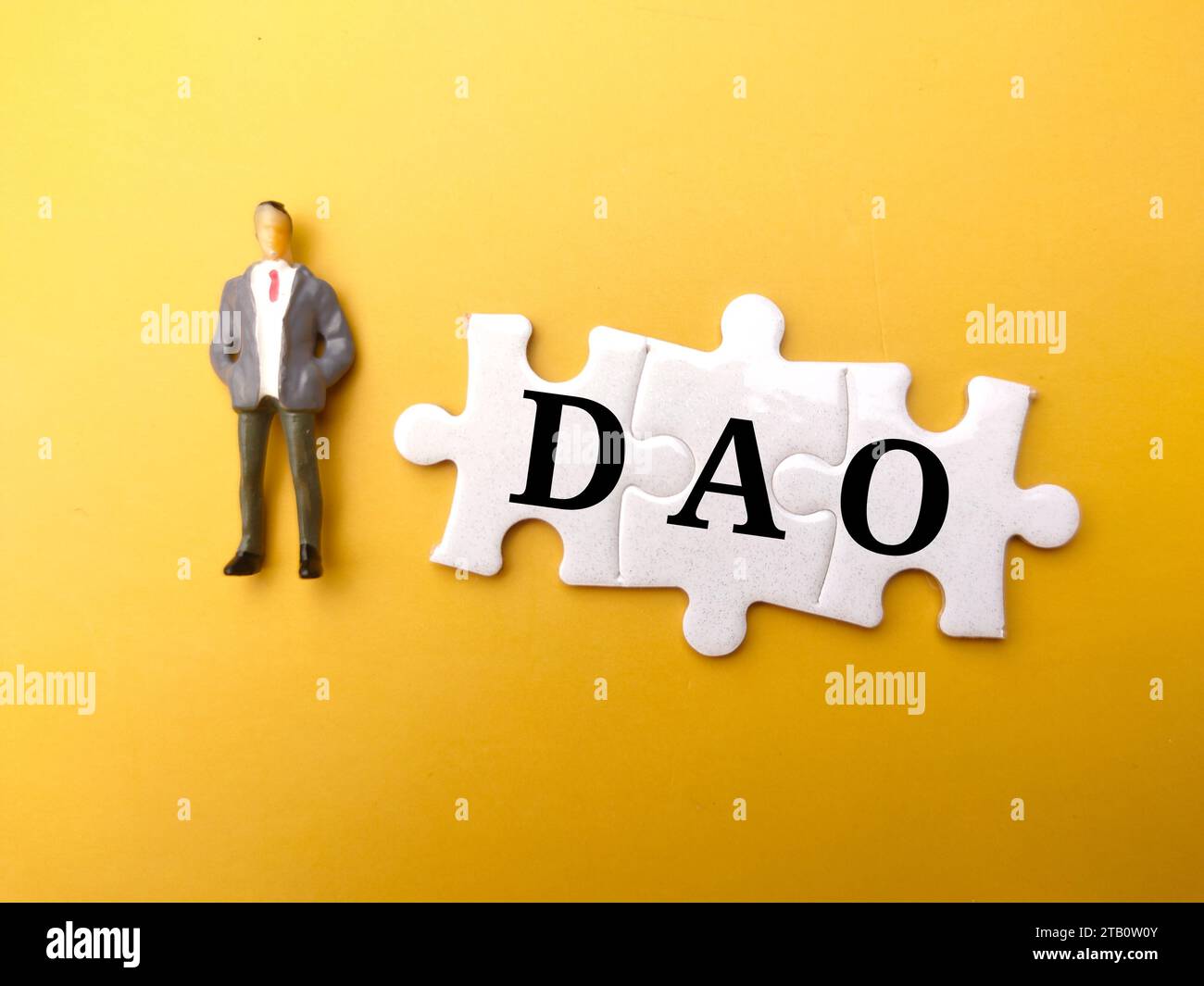 Miniature people and white puzzle with text DAO on yellow background