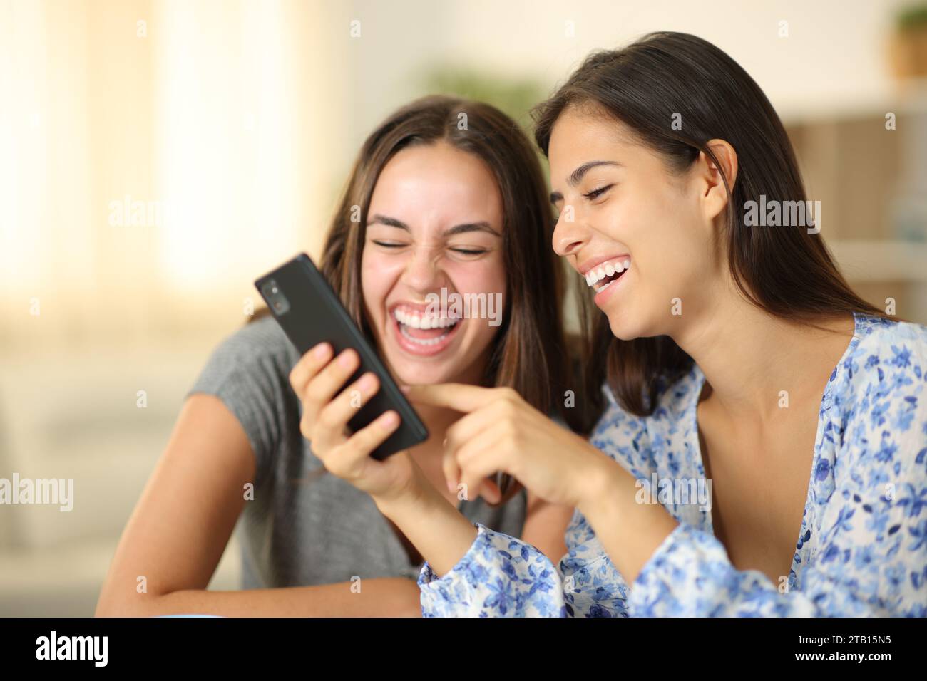 Two joyful roommates laughing watching media on phone at home Stock Photo