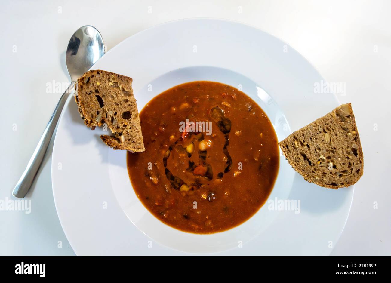 Bean and tomato soup with healthy seeded brown bread in a white bowl Stock Photo