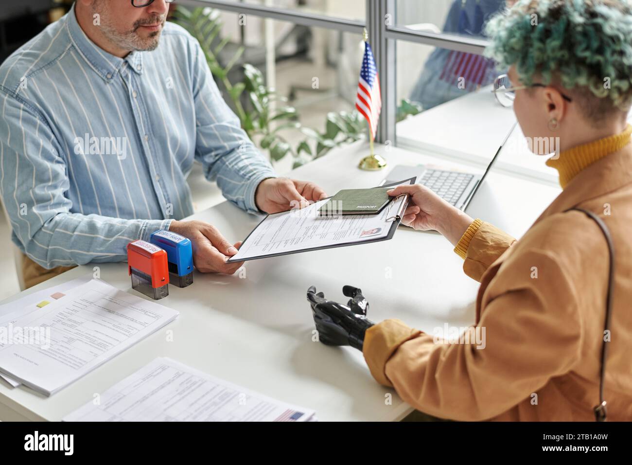Young woman with prosthetic arm giving documents to get visa in visa center Stock Photo