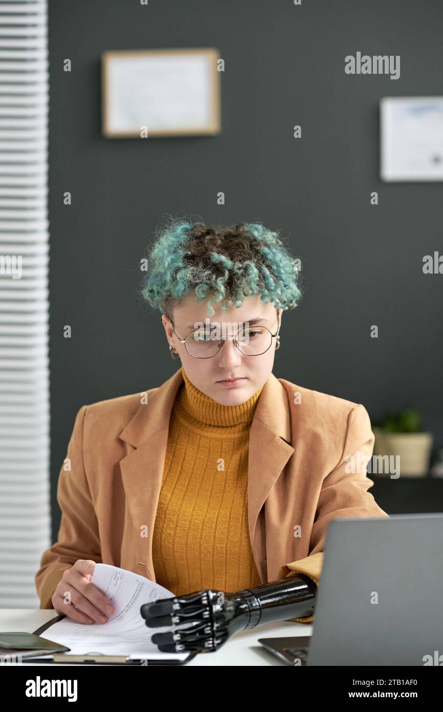 Vertical image of businesswoman with amputee arm doing paperwork in office Stock Photo