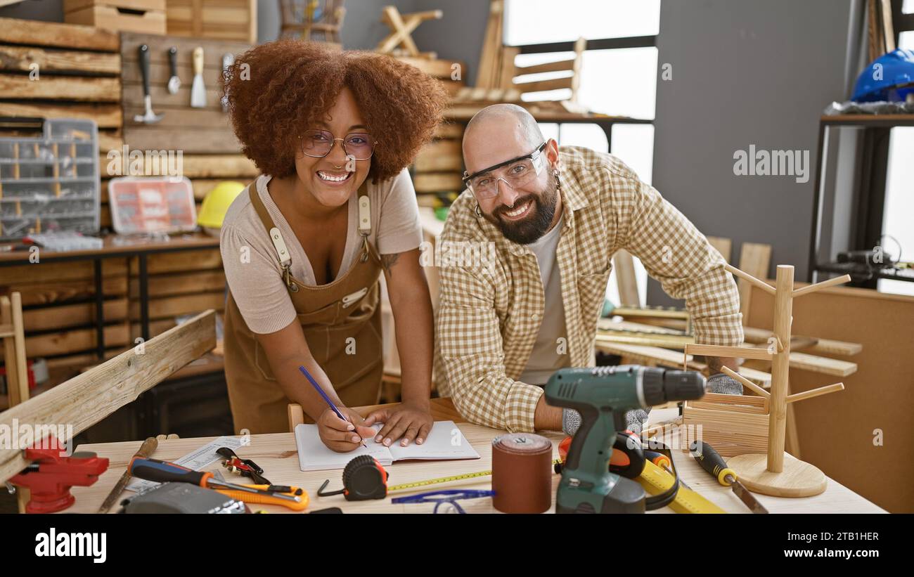 Two smiling carpenters confidently taking notes in their woodworking workshop Stock Photo
