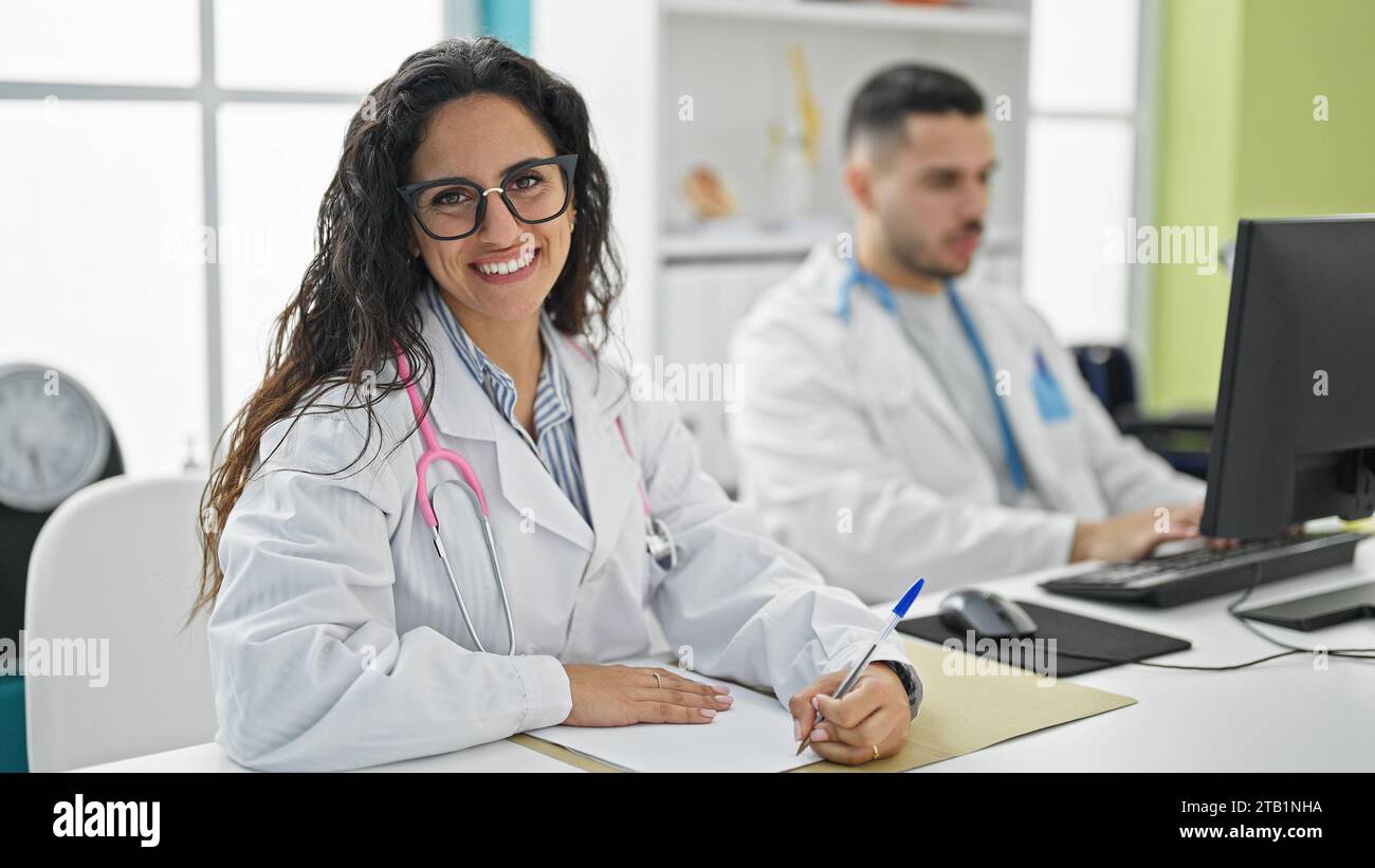 Man and woman doctors using computer taking notes smiling at the clinic Stock Photo