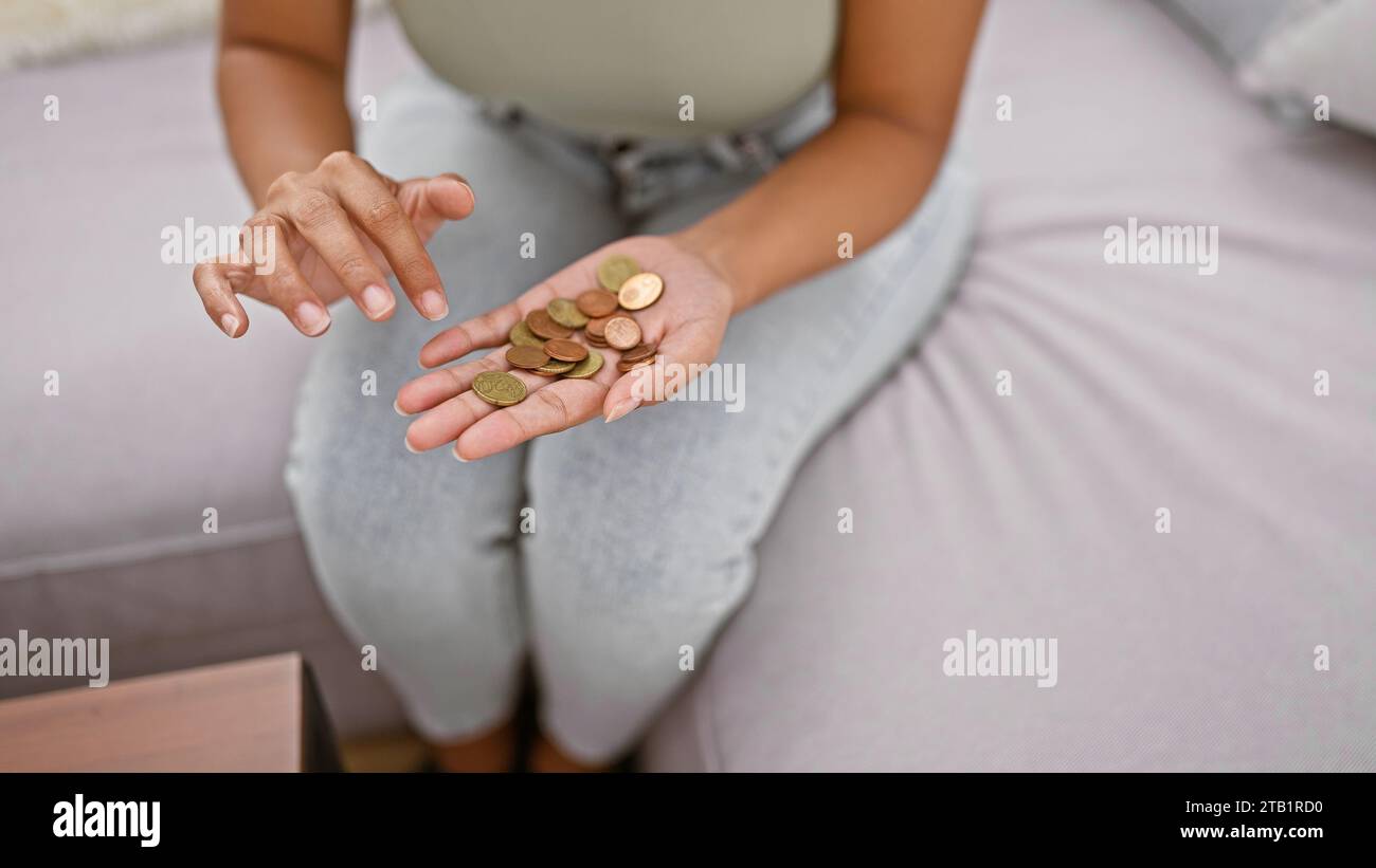 Close-up of a hardworking woman's hands carefully counting coins on a comfy sofa at home, maintaining her financial independence through savvy savings Stock Photo