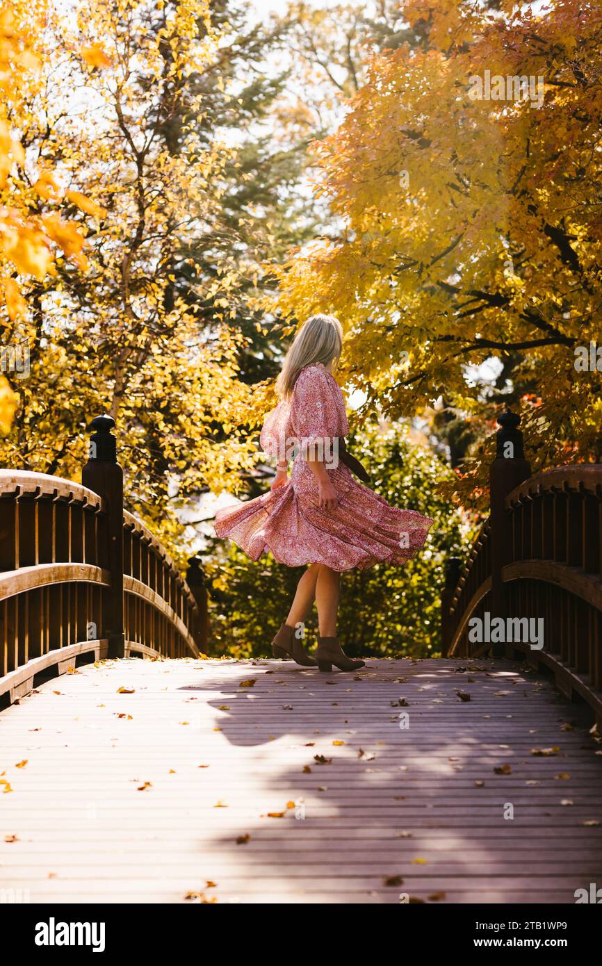Woman twirls dress on bridge in fall foliage forest Stock Photo