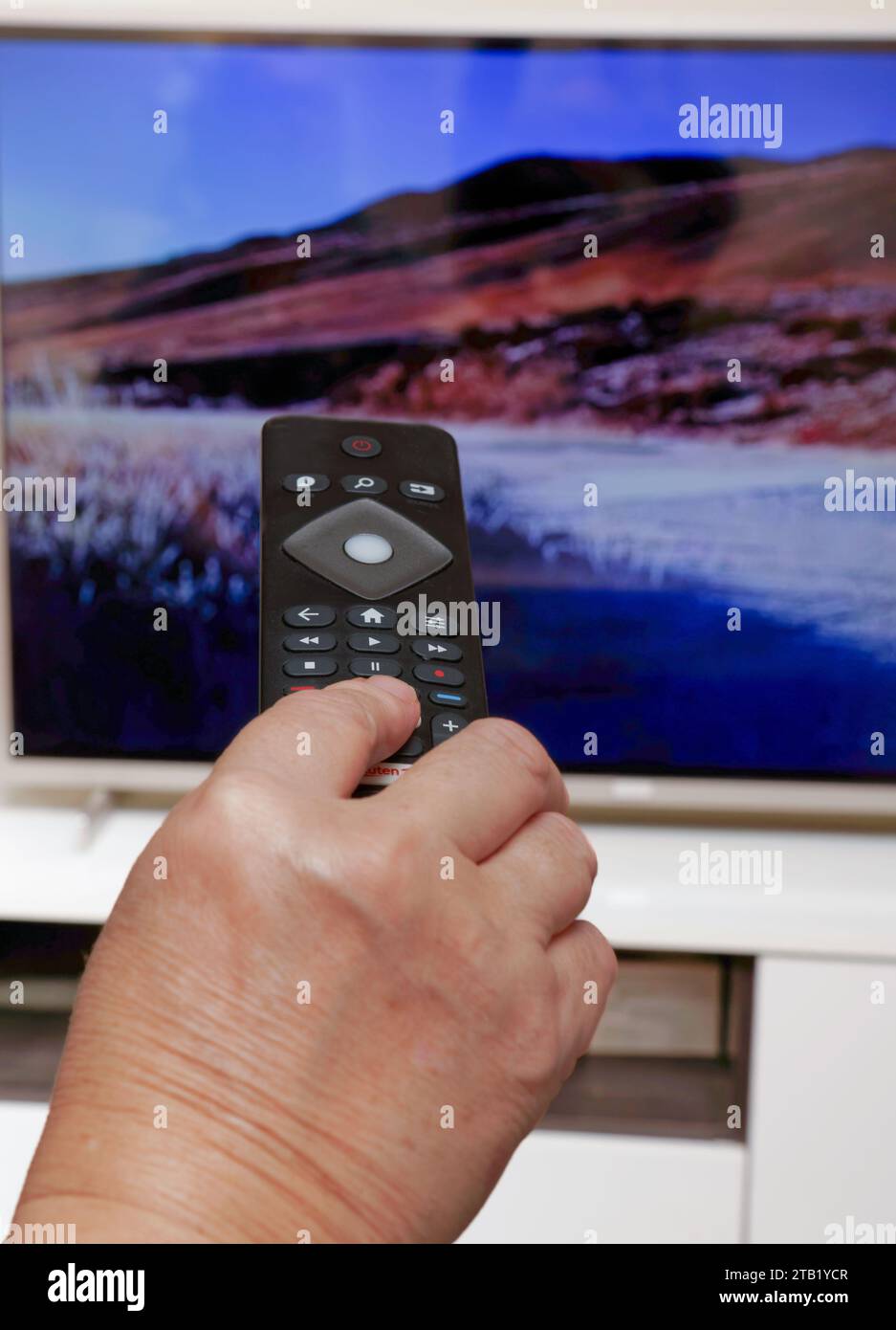 Woman with remote control in hand changing TV channels Stock Photo