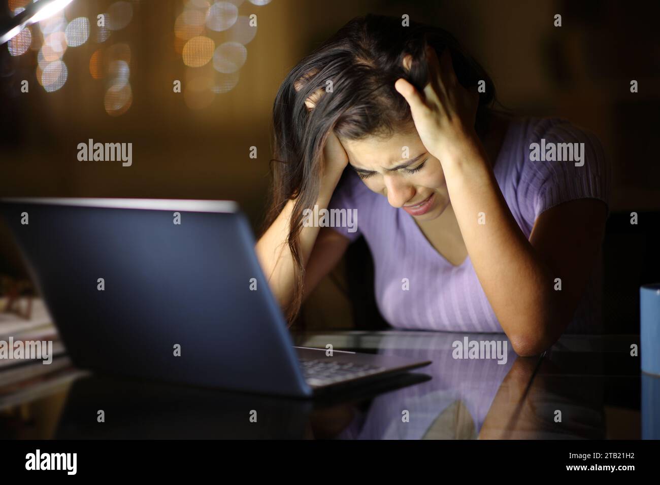 Sad woman complaining alone cheking laptop in the night at home Stock Photo