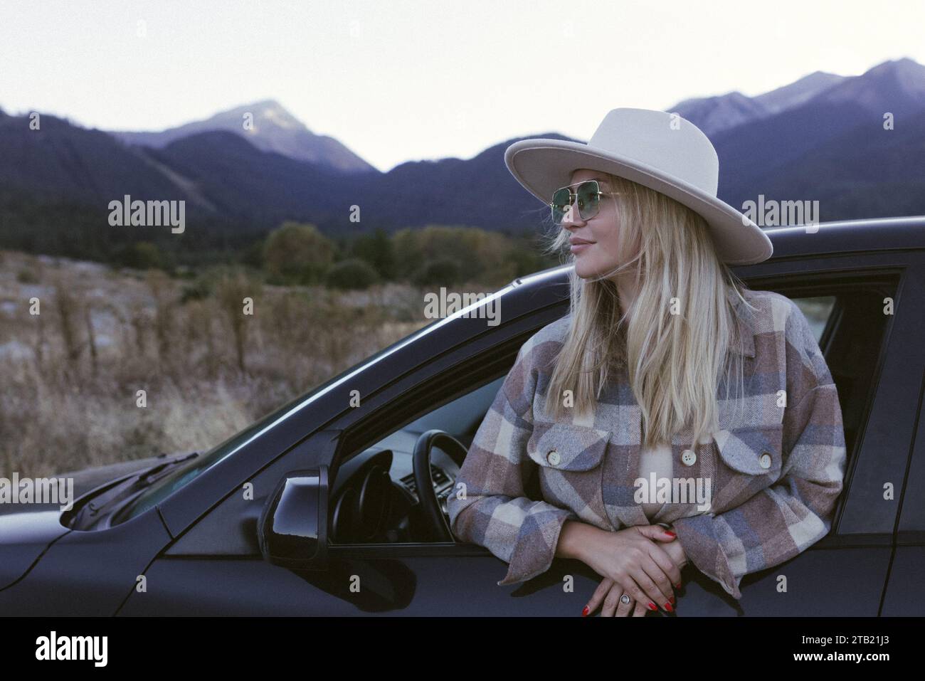 A woman traveler sits in a car against the background of mountains. Stock Photo