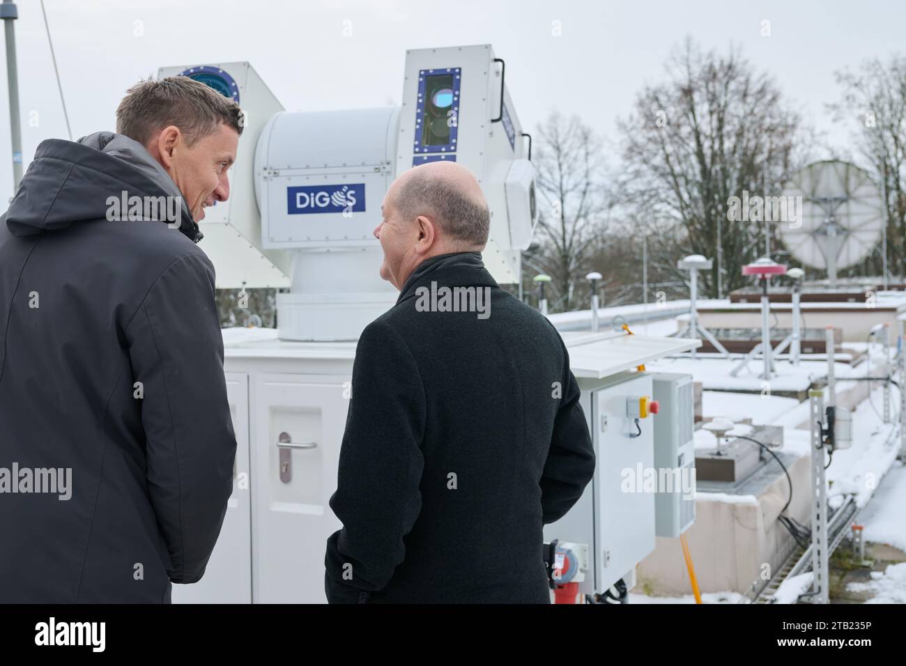 Potsdam, Germany. 04th Dec, 2023. Olaf Scholz (r, SPD), Federal Chancellor, stands on a terrace of the German Research Center for Geosciences (GFZ) as he inspects a laser ranging station for satellites of the GFZ spin-off DiGOS, which Andre Kloth (l), Managing Director of DiGOS, explains to him. The company Digos records satellites and space debris in space with millimeter precision. Scholz also visits the Potsdam Institute for Climate Impact Research (PIK) on Telegrafenberg to find out more about the energy transition. Credit: Annette Riedl/dpa/Alamy Live News Stock Photo
