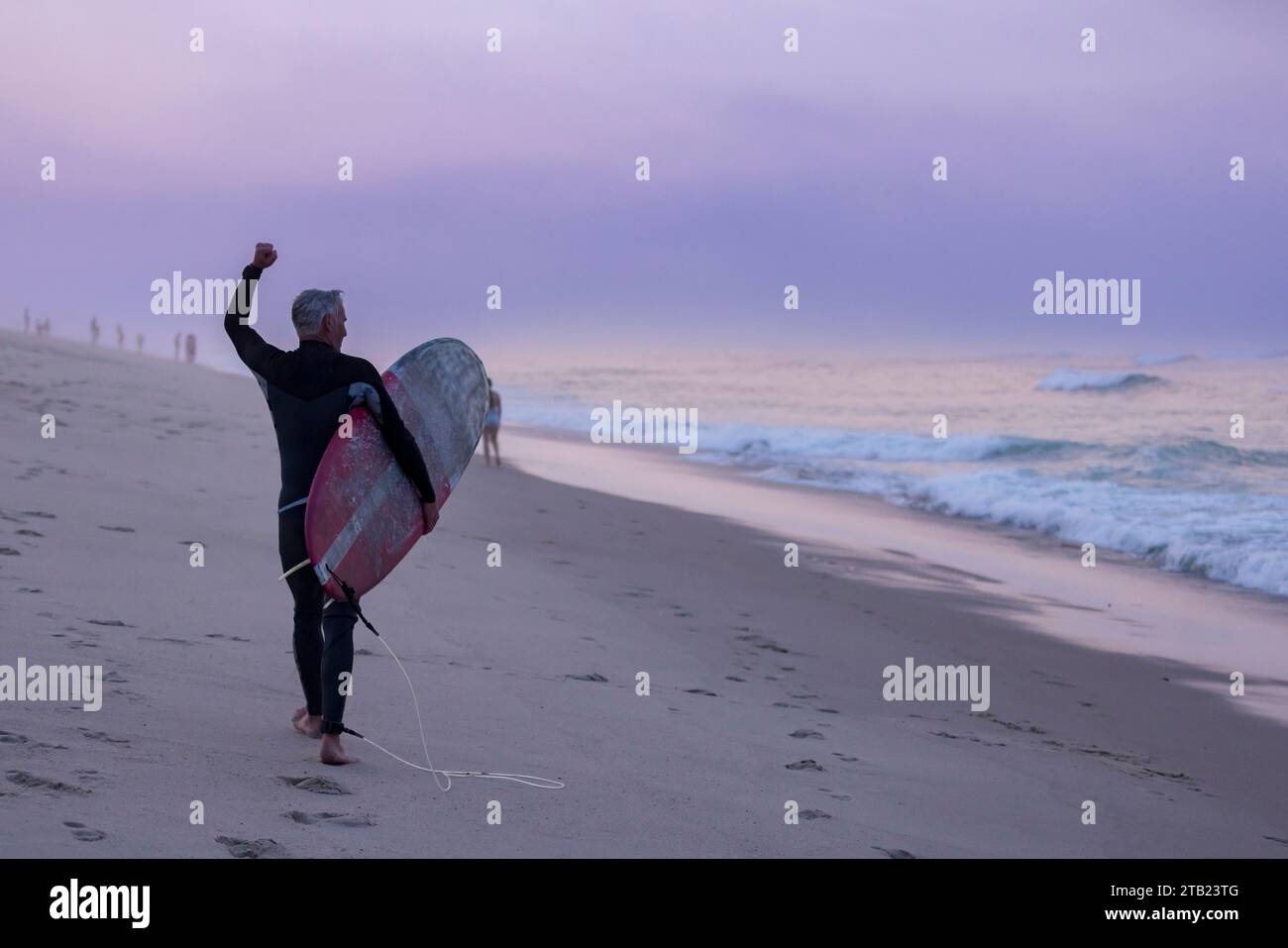 older surfer cheers on surfers on the beach at sunset on Cape Cod Stock ...
