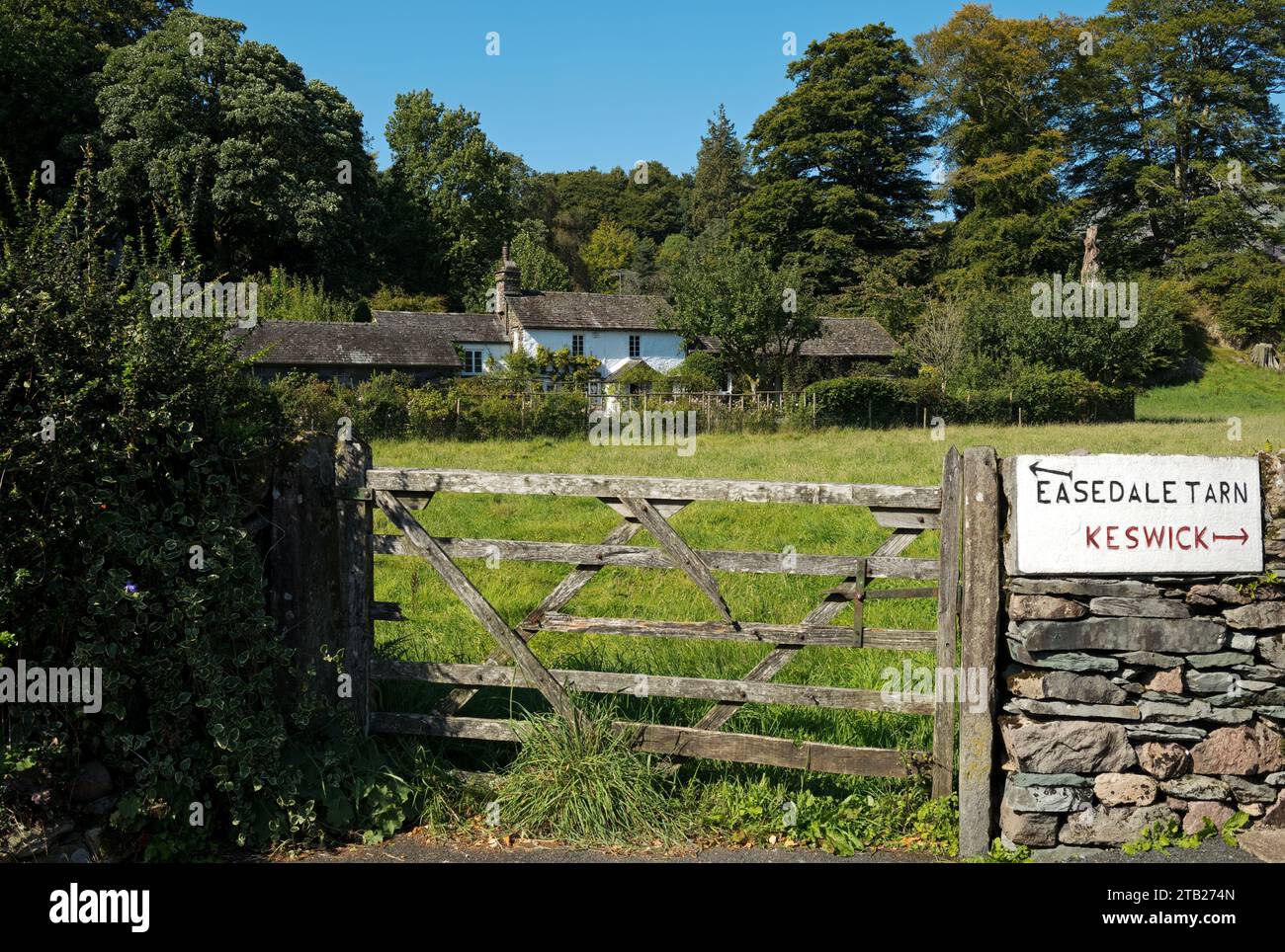 Old wooden farm gate and cottage near to a stone direction sign for Easedale Tarn and Keswick in summer Grasmere Cumbria England UK United Kingdom GB Stock Photo