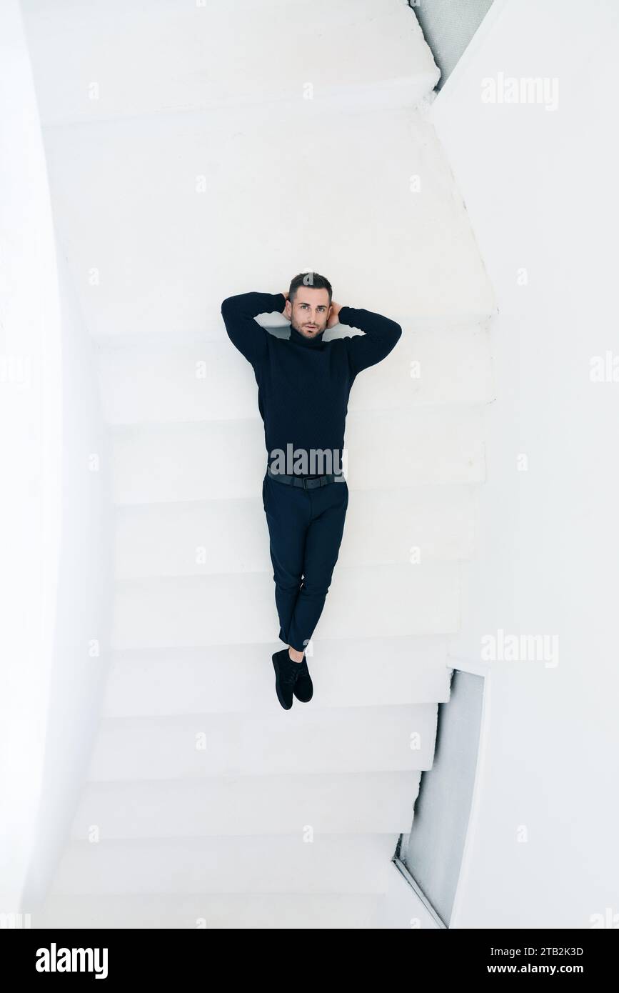 Young man in a black outfit lying on a white staircase. Top view Stock Photo