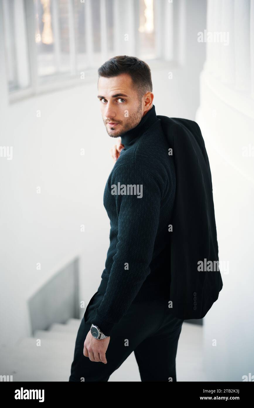 Fashionable man in a black stylish clothing outfit glancing back over bright sunlit architectural space. Male beauty Stock Photo