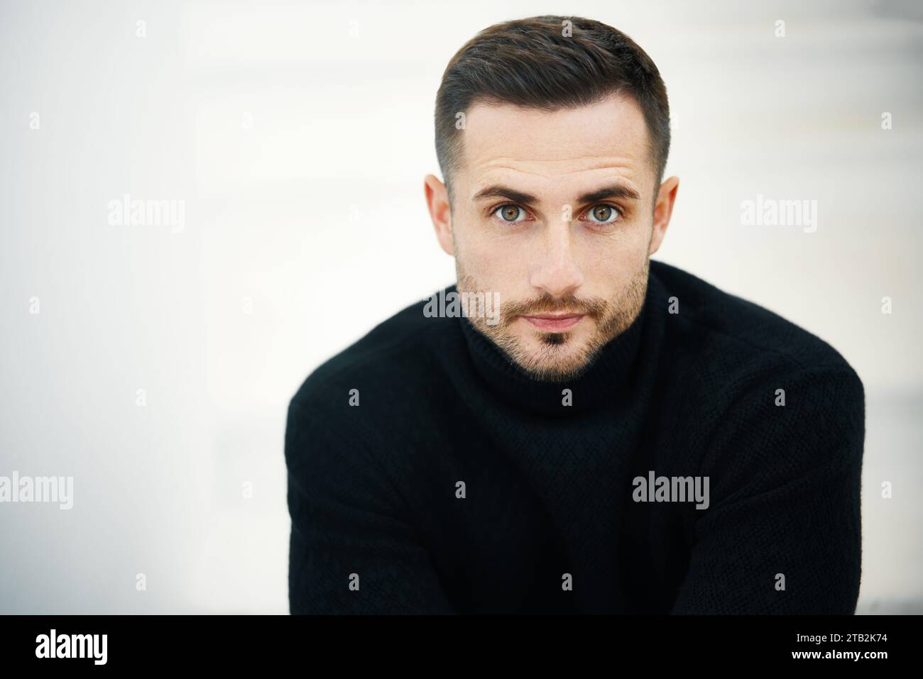 Close-up portrait of handsome young man wearing black turtleneck looking to camera over soft white background. Copy space. Male beauty concept Stock Photo