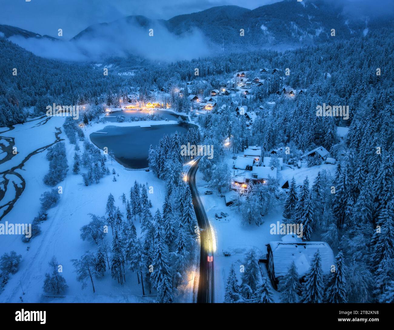 Aerial view of snowy village, trees, lake, street lights at night Stock ...