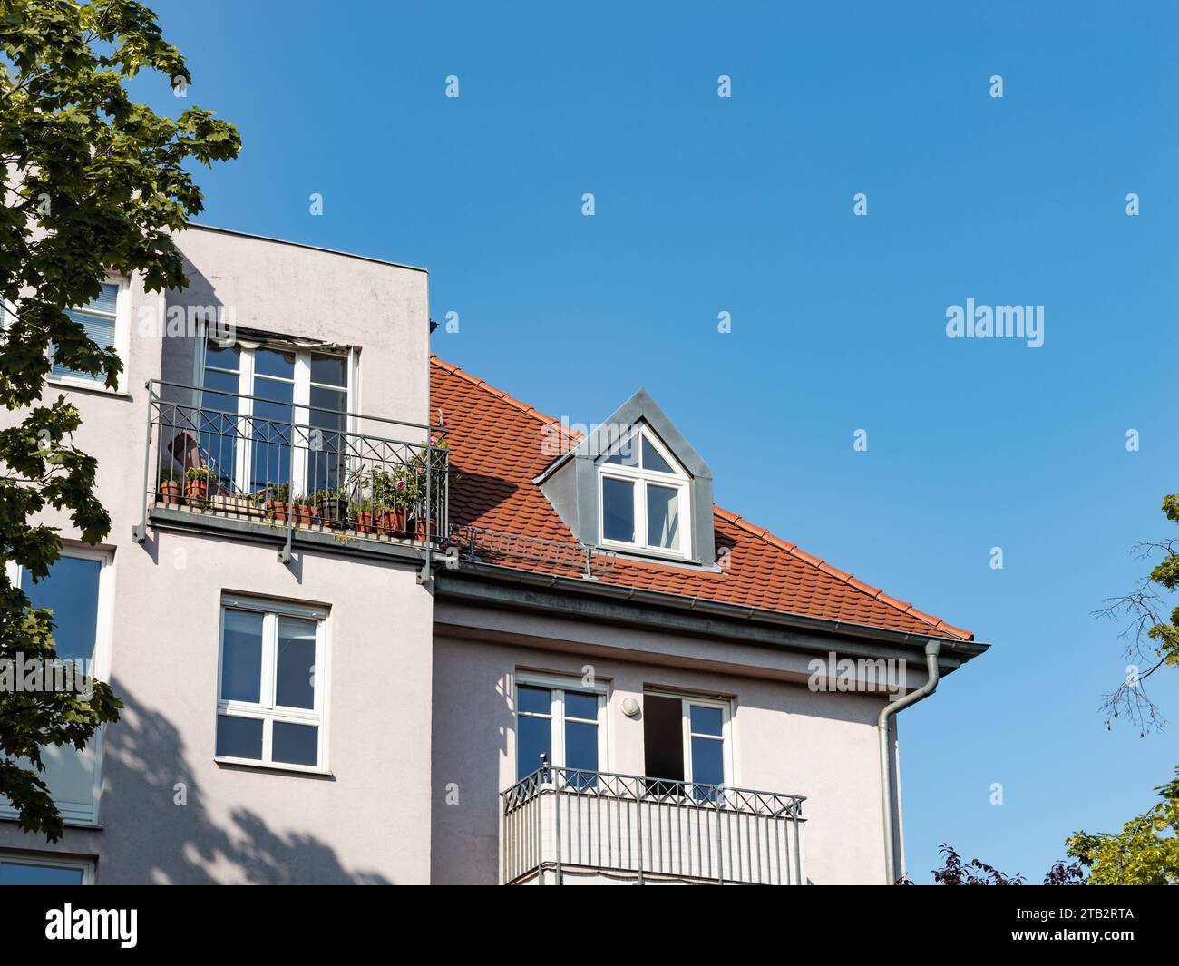 Building exterior with a dormer window on the rooftop. Balconies on the house facade. Apartment building with multiple dwellings is real estate. Stock Photo