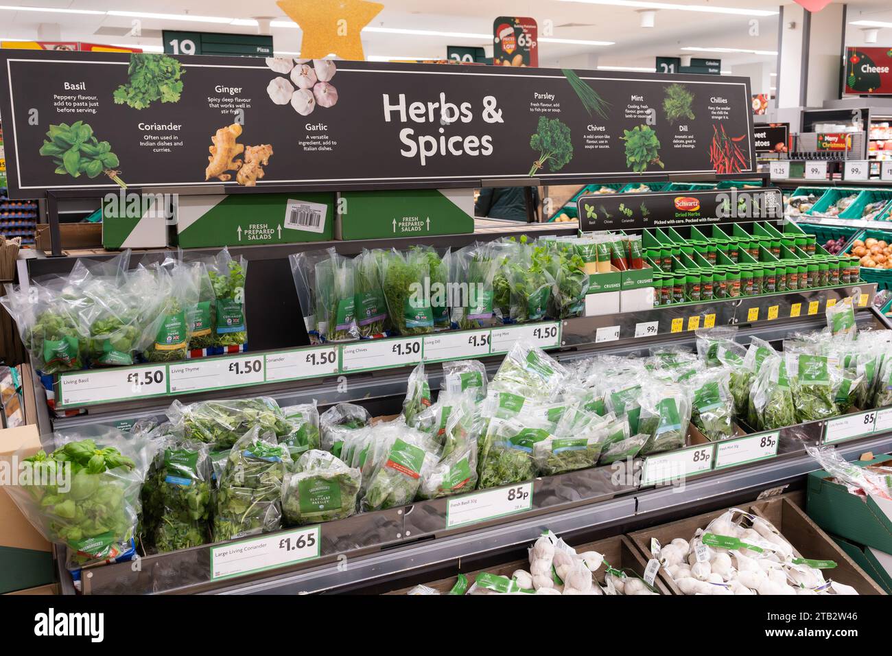 Herbs and spices display with prices for fresh herbs in packets and jars and an advertising sign above at a Morrisons supermarket, UK Stock Photo