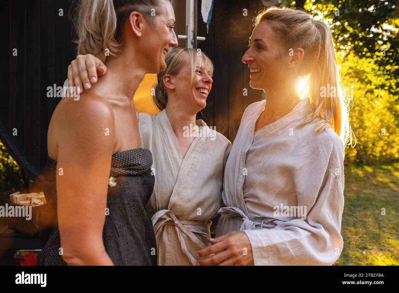 Three happy people in robes by a Finnish sauna barrel, laughing and chatting Stock Photo