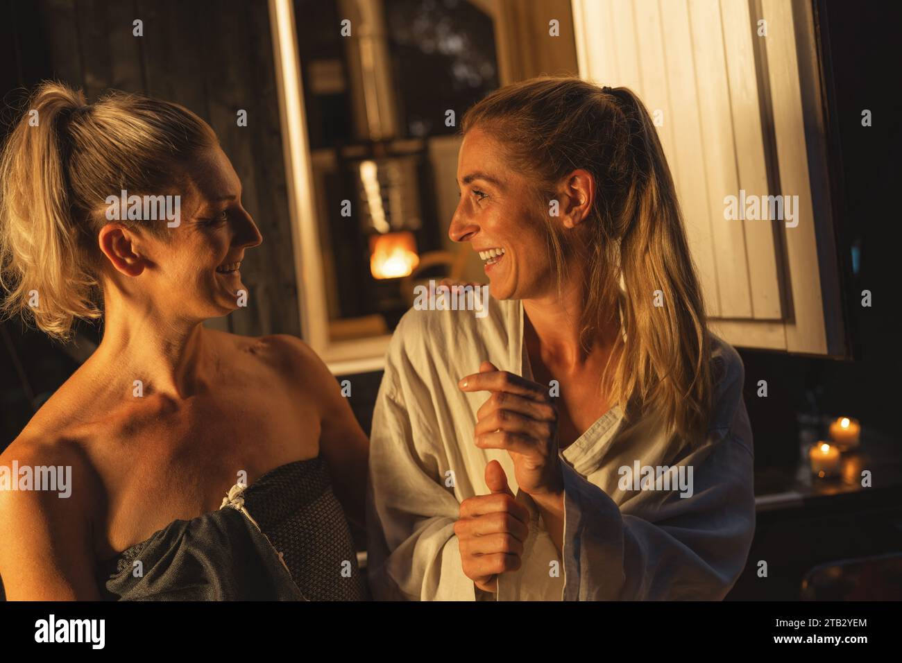 Two smiling women sitting at the entrance of a Finnish barrel sauna, enjoying the moment. Stock Photo