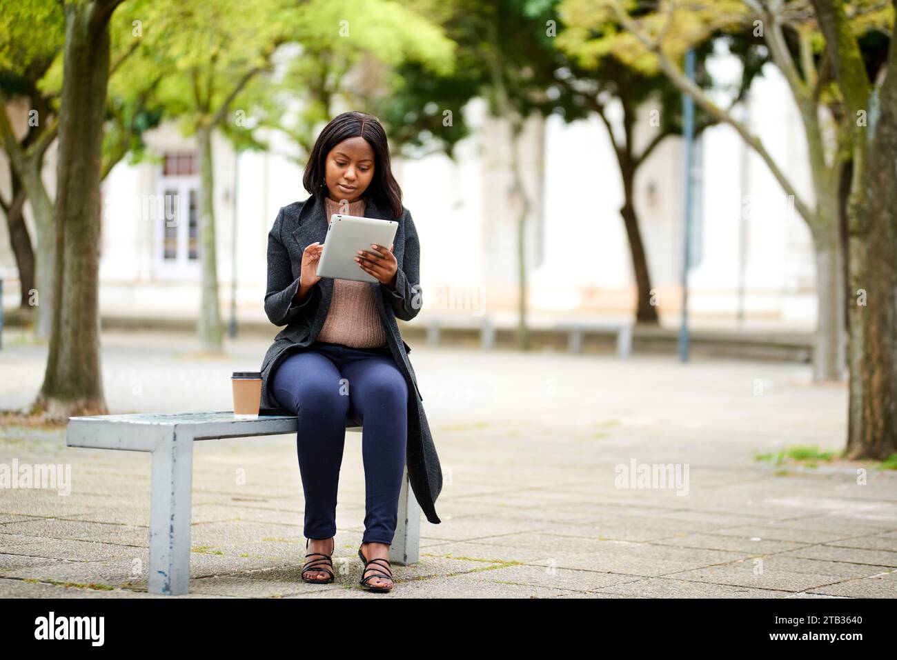 Young Black career woman sitting on outdoor bench with tablet, smiling Stock Photo