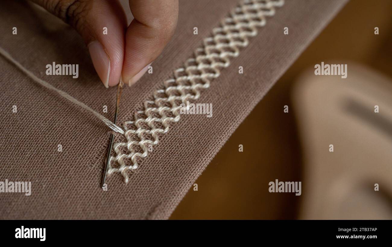 Artistry in Stitches: Woman's Hand Embroidering Brown Fabric Stock Photo