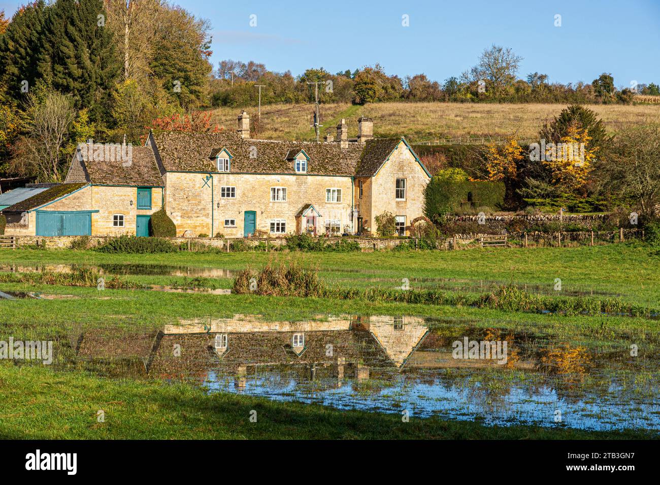 Stowell Mill (or Yanworth Mill) reflected in flood water from the infant River Coln near the Cotswold village of Yanworth, Gloucestershire, England UK Stock Photo