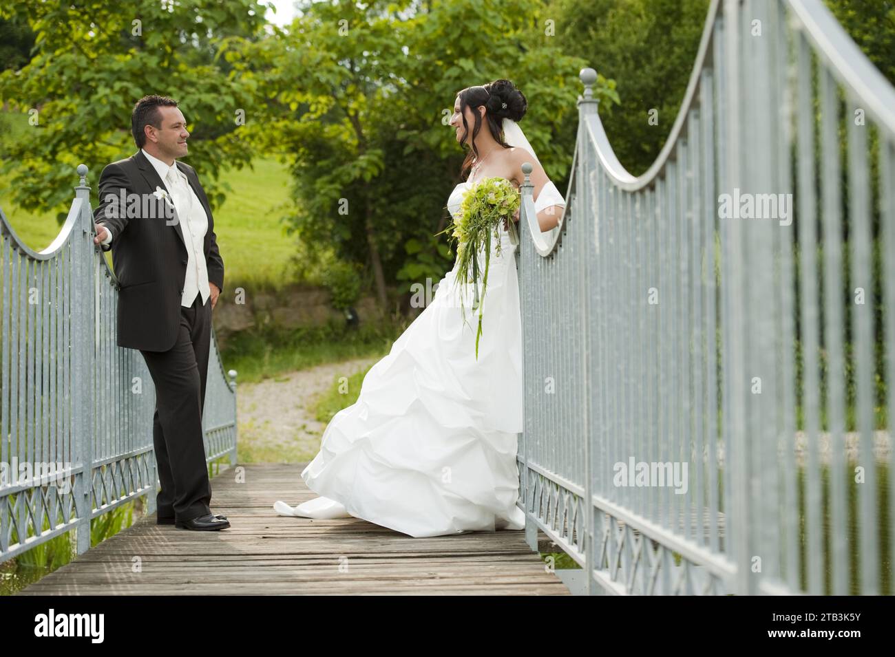 Romantisches Brautpaar am Parkeingang - weisses Tor, Mann, Frau, Anzugträger, Brautkleid, Blumen, Brautstrauss, Stock Photo