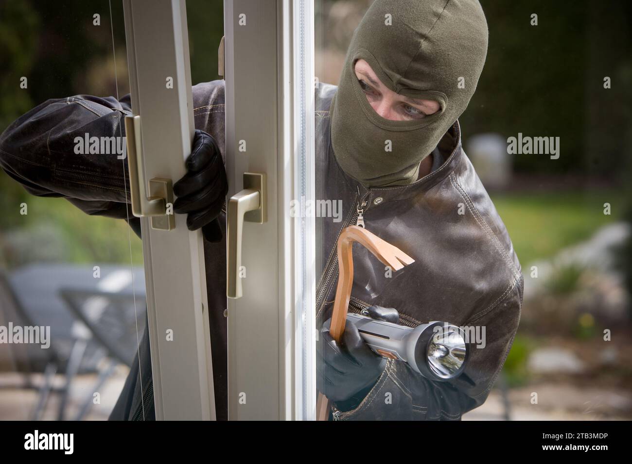Ein maskierter Einbrecher mit einer Taschenlampe öffnet ein Fenster, Einbruch, Diebstahl, Stock Photo