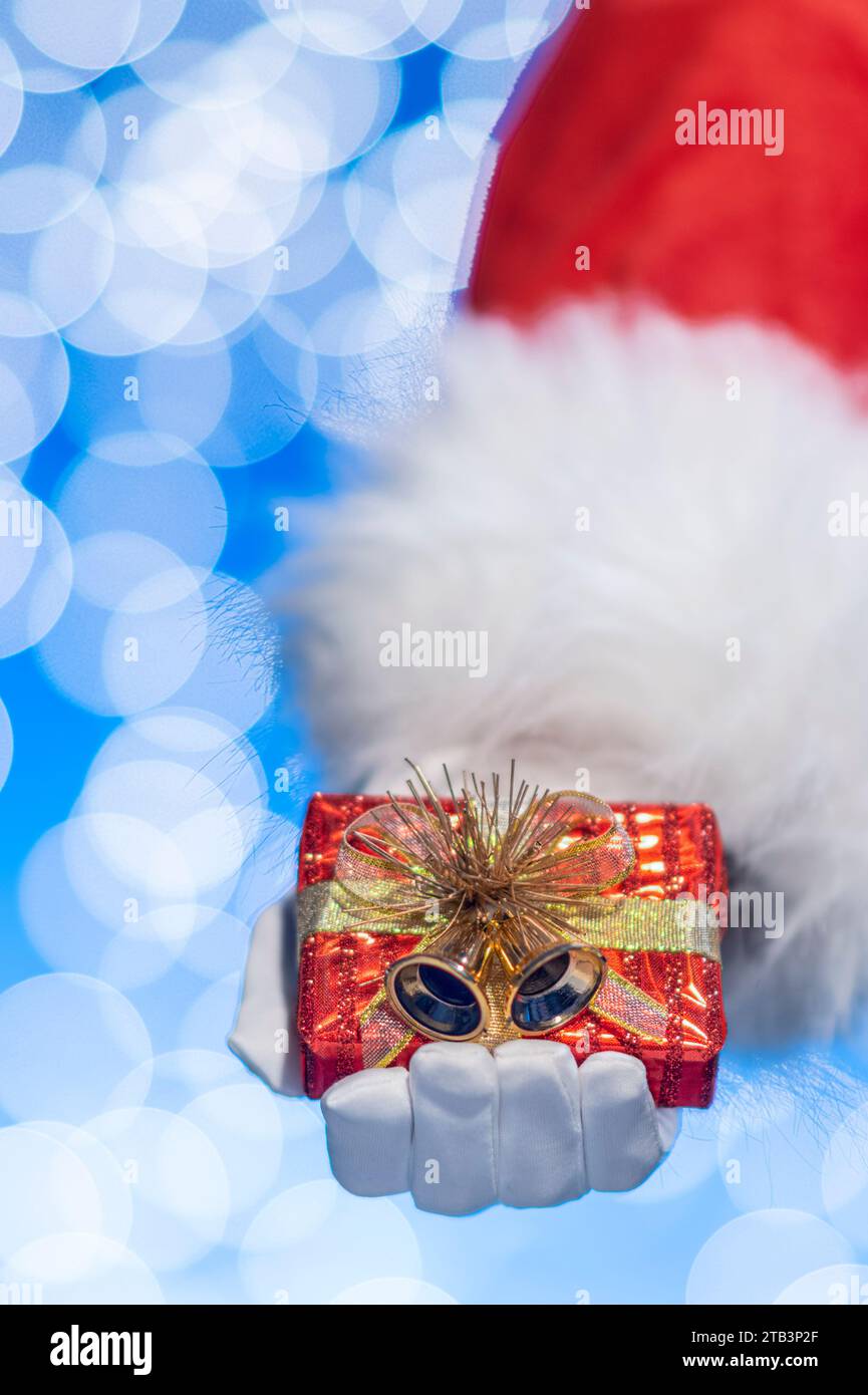 A close-up of Santa Claus holding a small red wrapped gift with gold ...