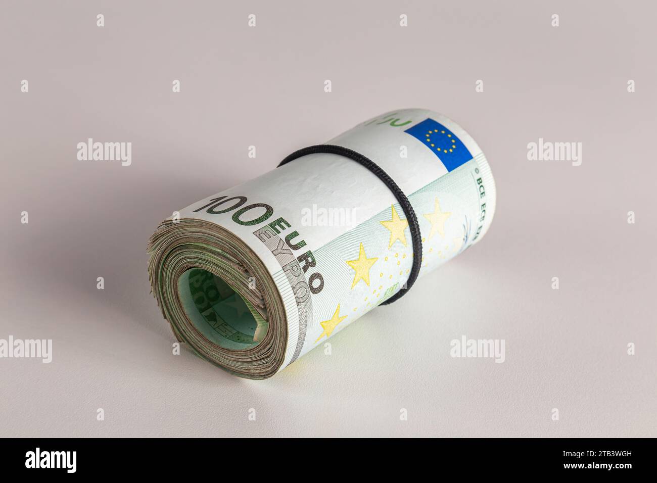 A roll of one hundred euro banknotes lie on a table on a light ...