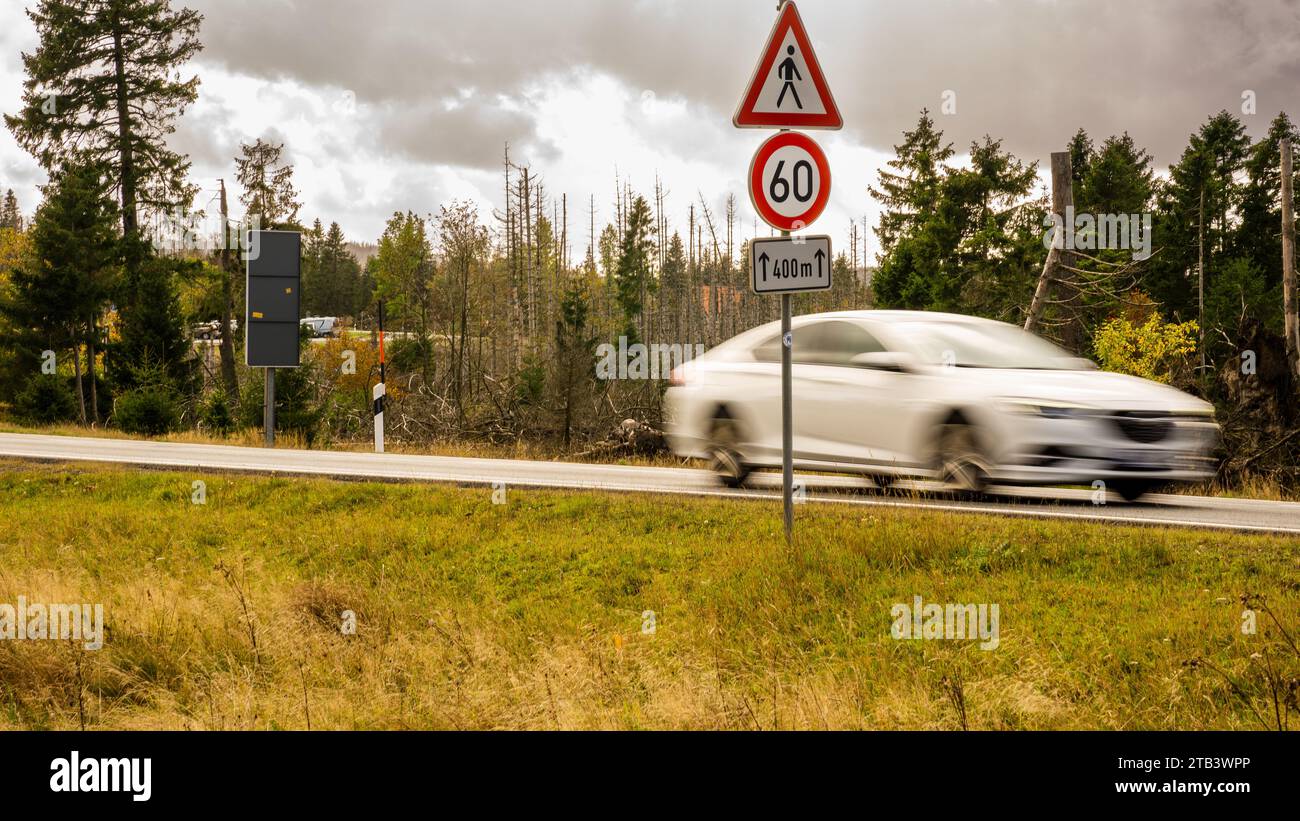 White car driving fast on the land streets in the middle of the national forest in Harz lower saxony in a speed limit zone of 60 km/h on day Stock Photo