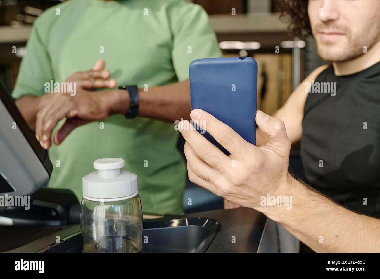 Unknown caucasian guy showing smartphone to unrecognizable black man standing on treadmill at gym Stock Photo