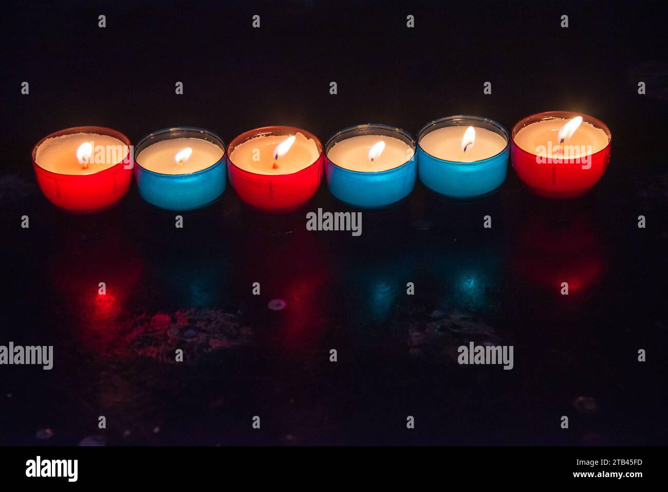 Burning candles in the church. Raw of colorful red blue burning candles in dark. Religious holiday celebration background.  Hope, pray concepts. Stock Photo