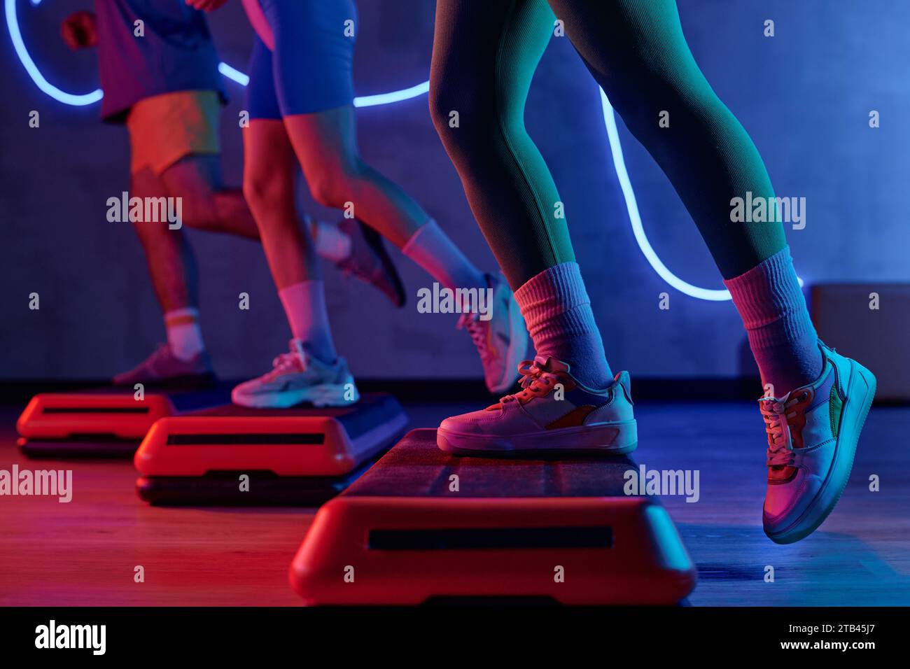 Unknown gym goer stepping onto step platform with one leg with sportspeople exercising on