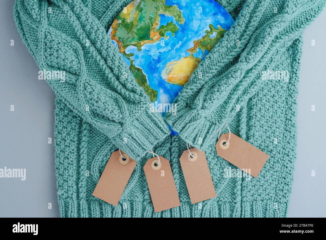 Sleeves of knitwear sweater hug the planet with tags. Responsible consumption clothes. Environmental friendliness and sustainable fashion. Stock Photo