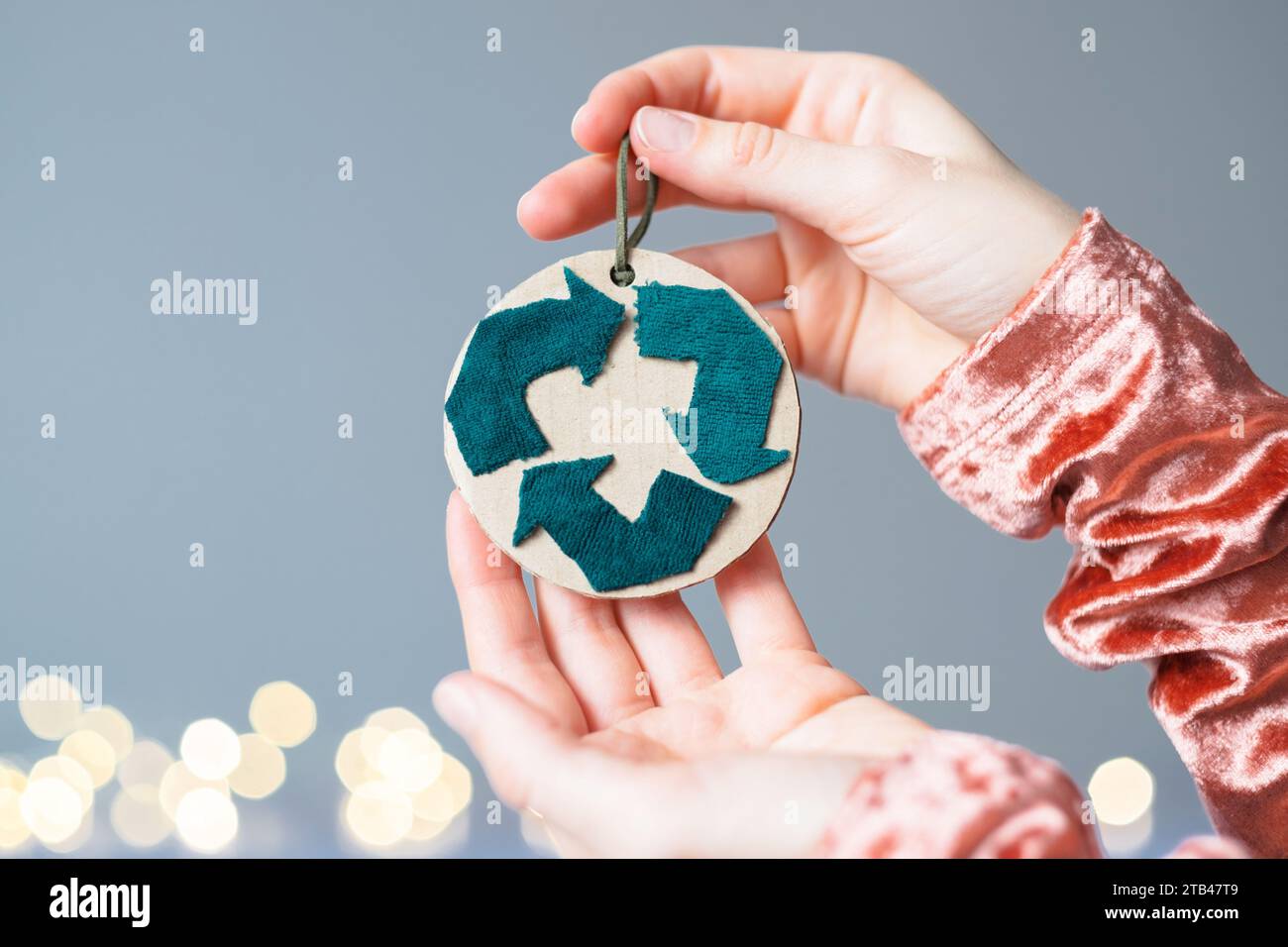 Creative symbol of clothing recycling. A woman holding a eco Christmas tree decoration on the background lights. Clothing recycling. Stock Photo