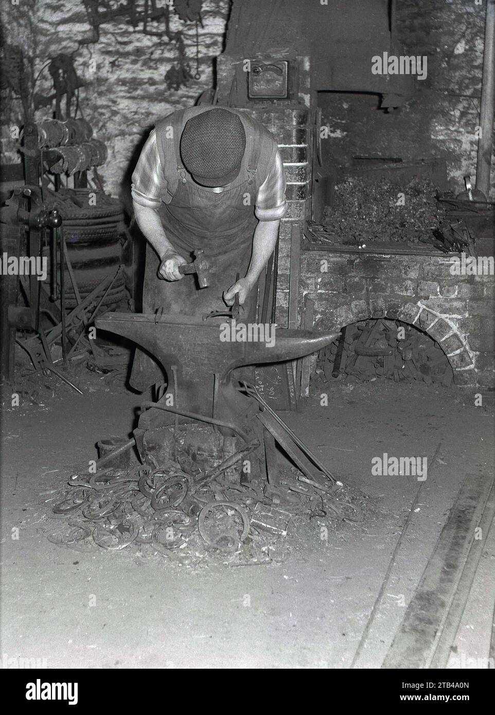 1970s, historical, a farrier in an stone barn working at an anvil ...