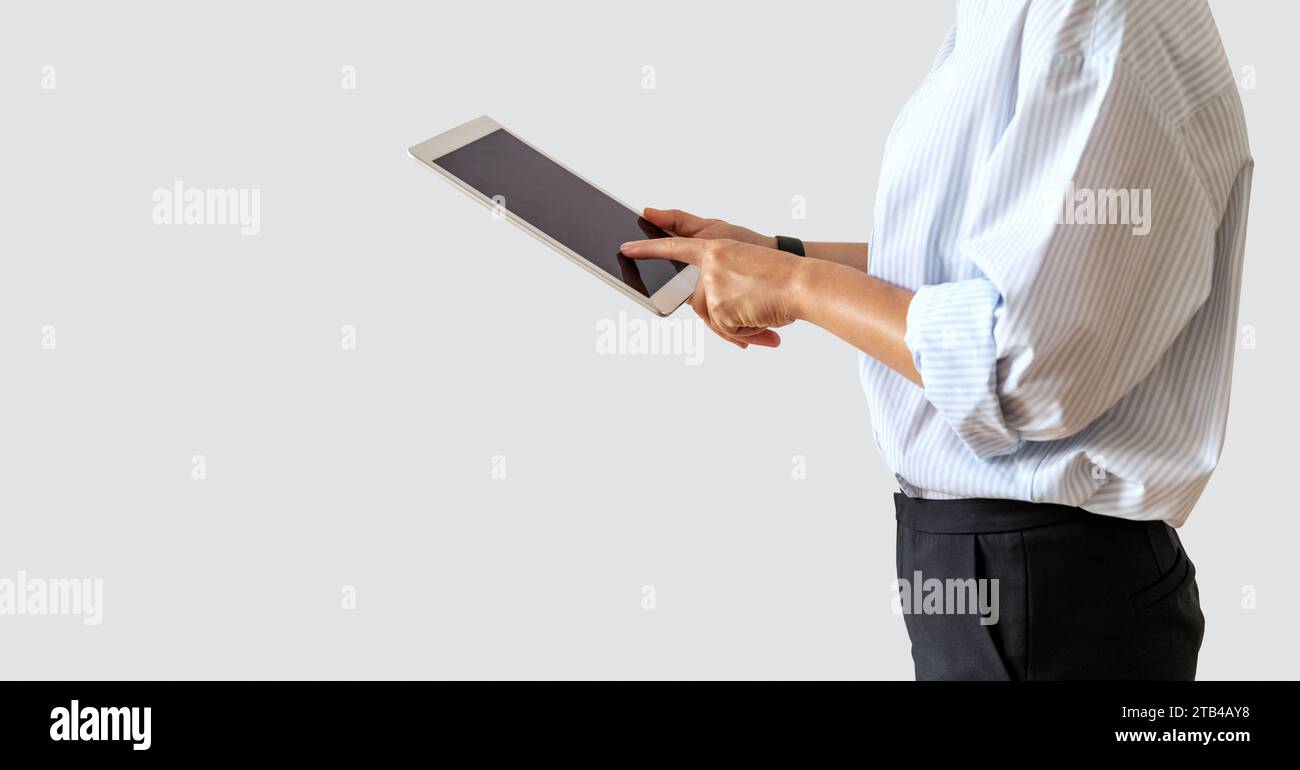 Female business person wearing formal outfit using digital tablet, touching blank screen with her finger in front of plain background. E-commercial an Stock Photo